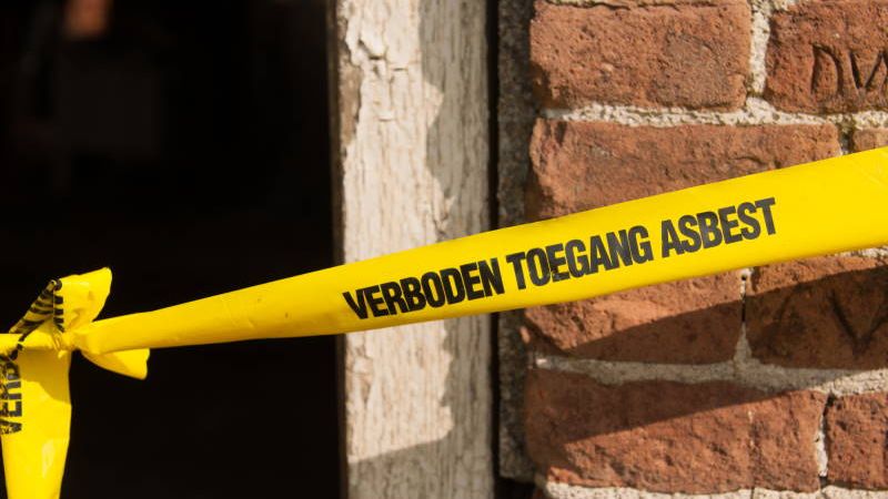 Gele afzetlint met de tekst verboden toegang asbest voor een bakstenen gevel